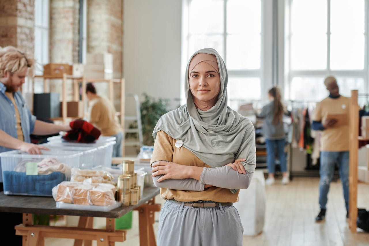 Portrait of a woman in hijab volunteering at a donation center with diverse helpers.
